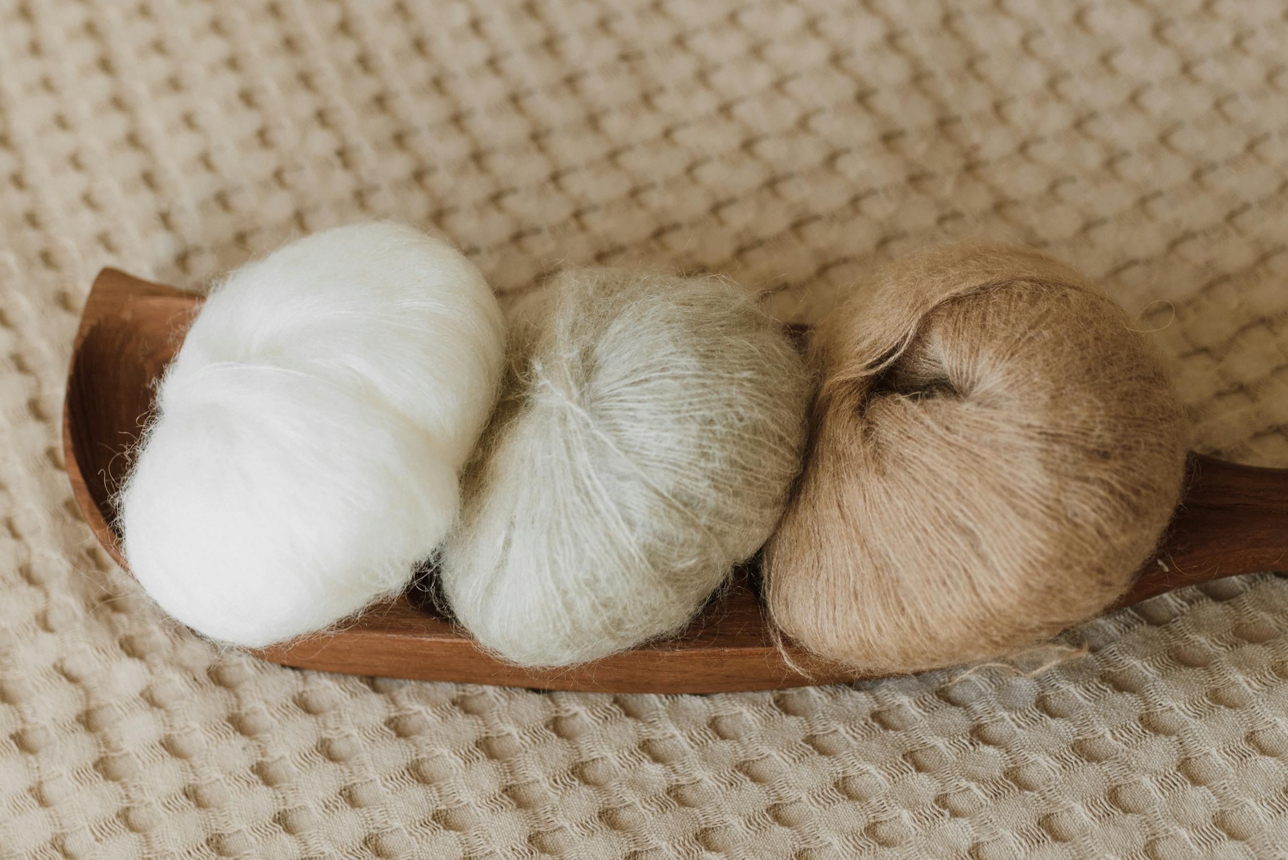 Three wool yarn balls in neutral tones placed on an elegant wooden tray.